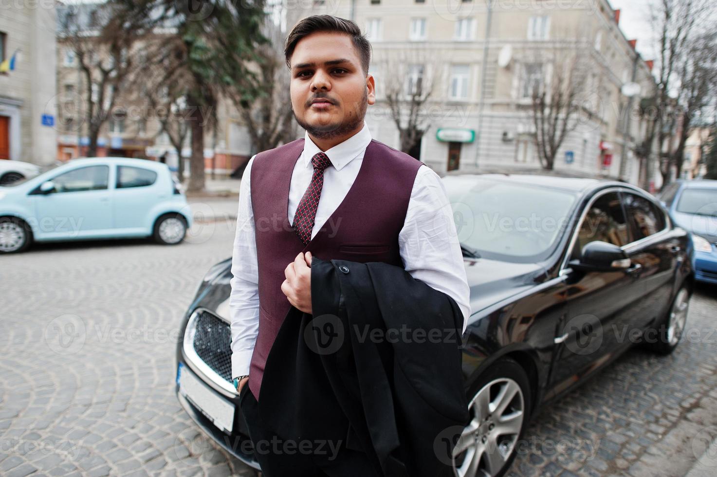 Stylish indian businessman in formal wear standing against black business car on street of city. photo