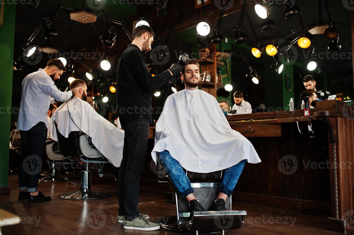 Handsome bearded man at the barbershop, barber at work, using hair dryer. photo