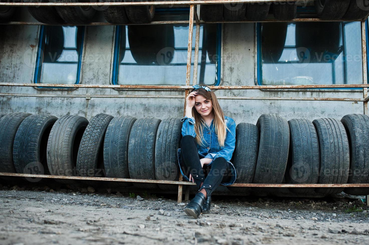 joven hipster con chaqueta de jeans y pañuelo en la cabeza en la zona de montaje de neumáticos. foto