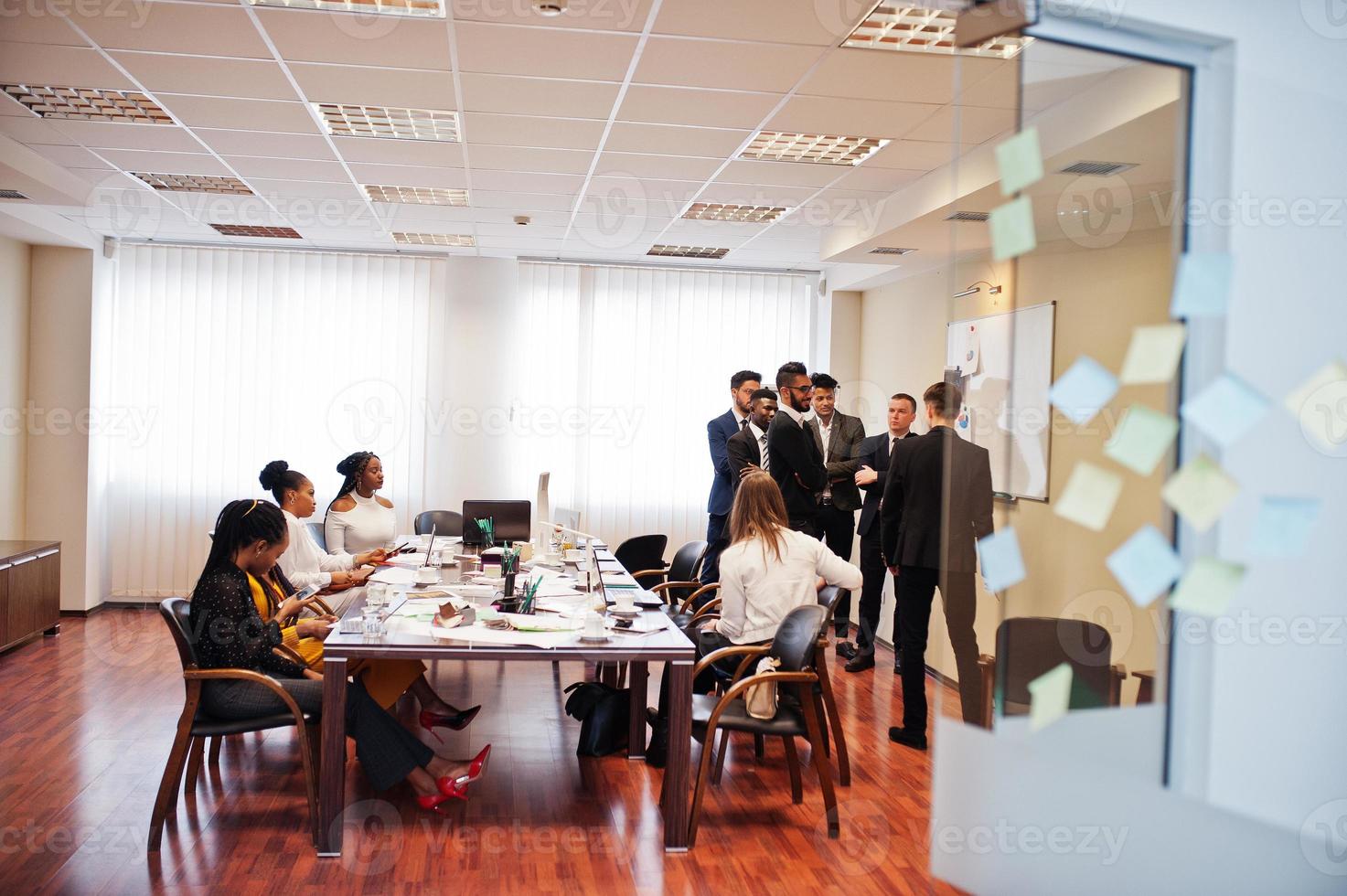 el equipo de negocios multirracial se dirige a la reunión alrededor de la mesa de juntas y escribe el plan a bordo. foto