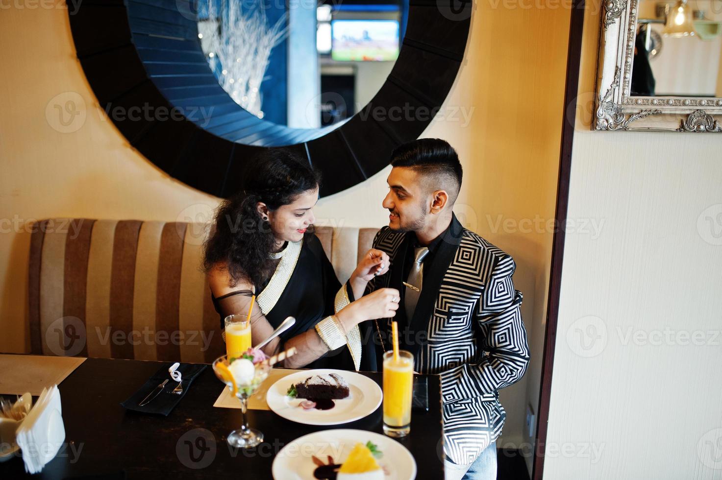 Lovely indian couple in love, wear at saree and elegant suit, posed on restaurant. Woman tied tie on her man. photo