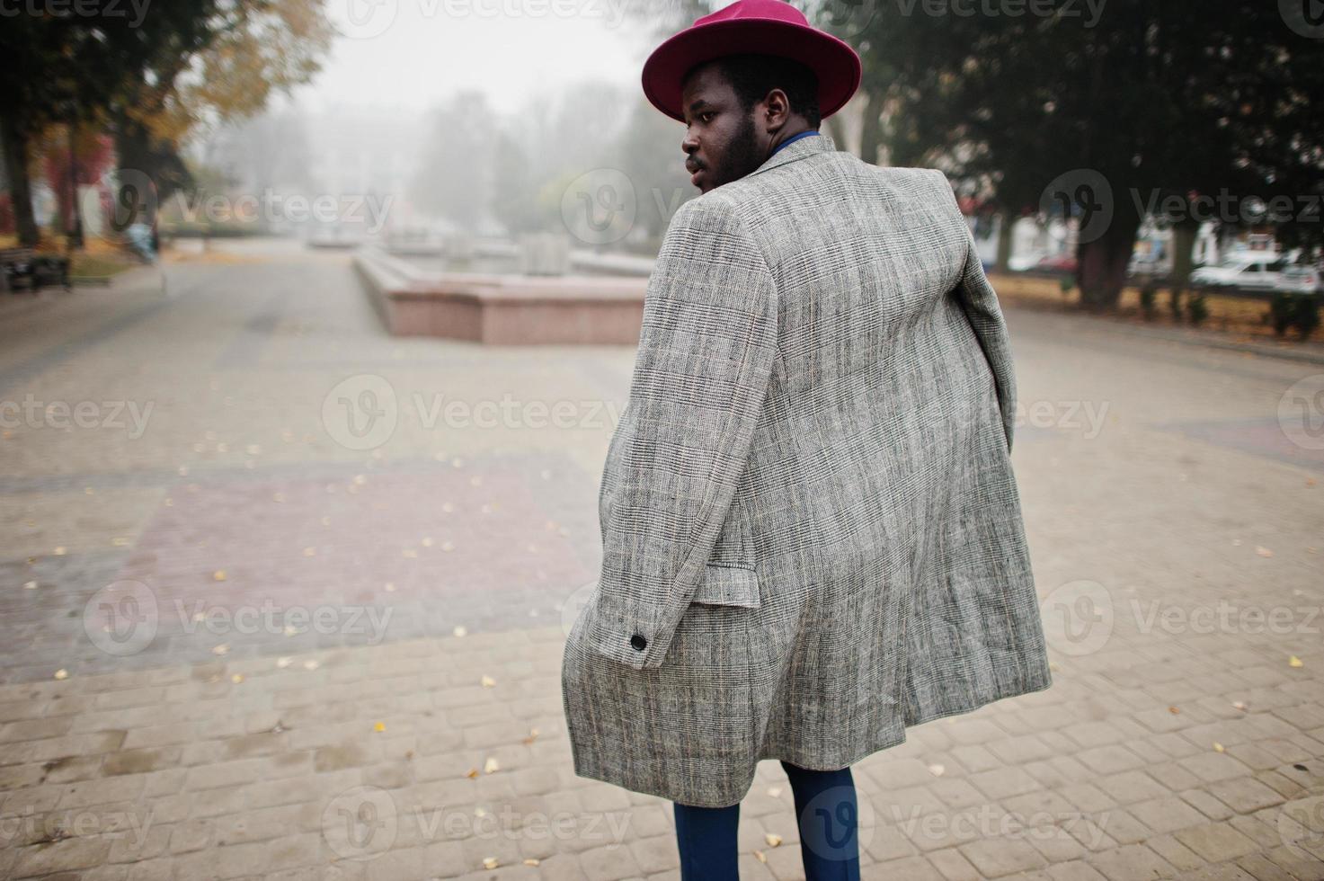Stylish African American man model in gray coat, jacket tie and red hat walking at foggy weather street. photo