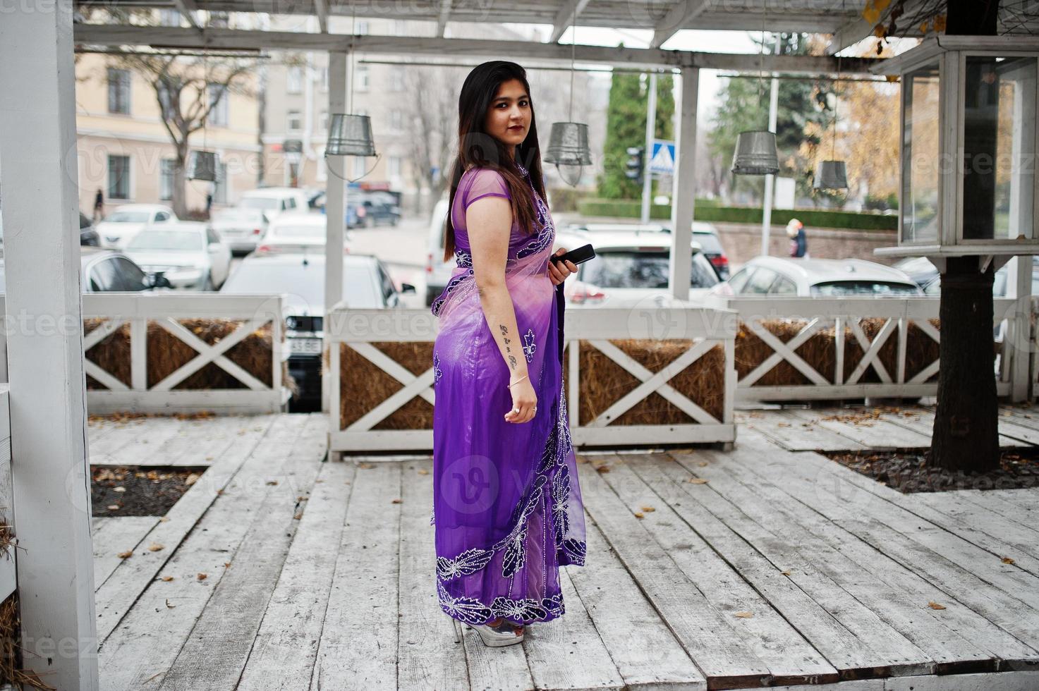 Indian hindu girl at traditional violet saree posed at street against wooden terrace. photo