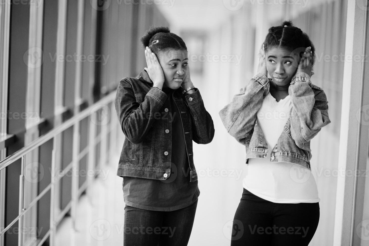 dos amigas africanas con chaqueta de jeans cubrieron sus oídos con las manos juntas en el interior. foto