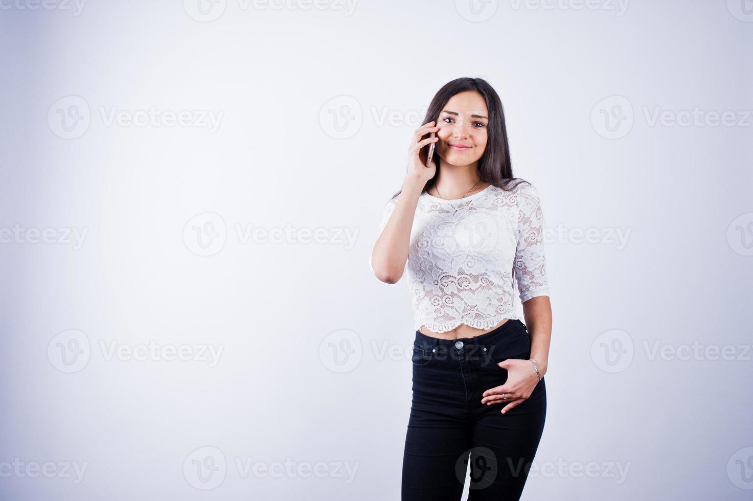 retrato de una mujer joven y hermosa con top blanco y pantalón negro usando su teléfono. foto