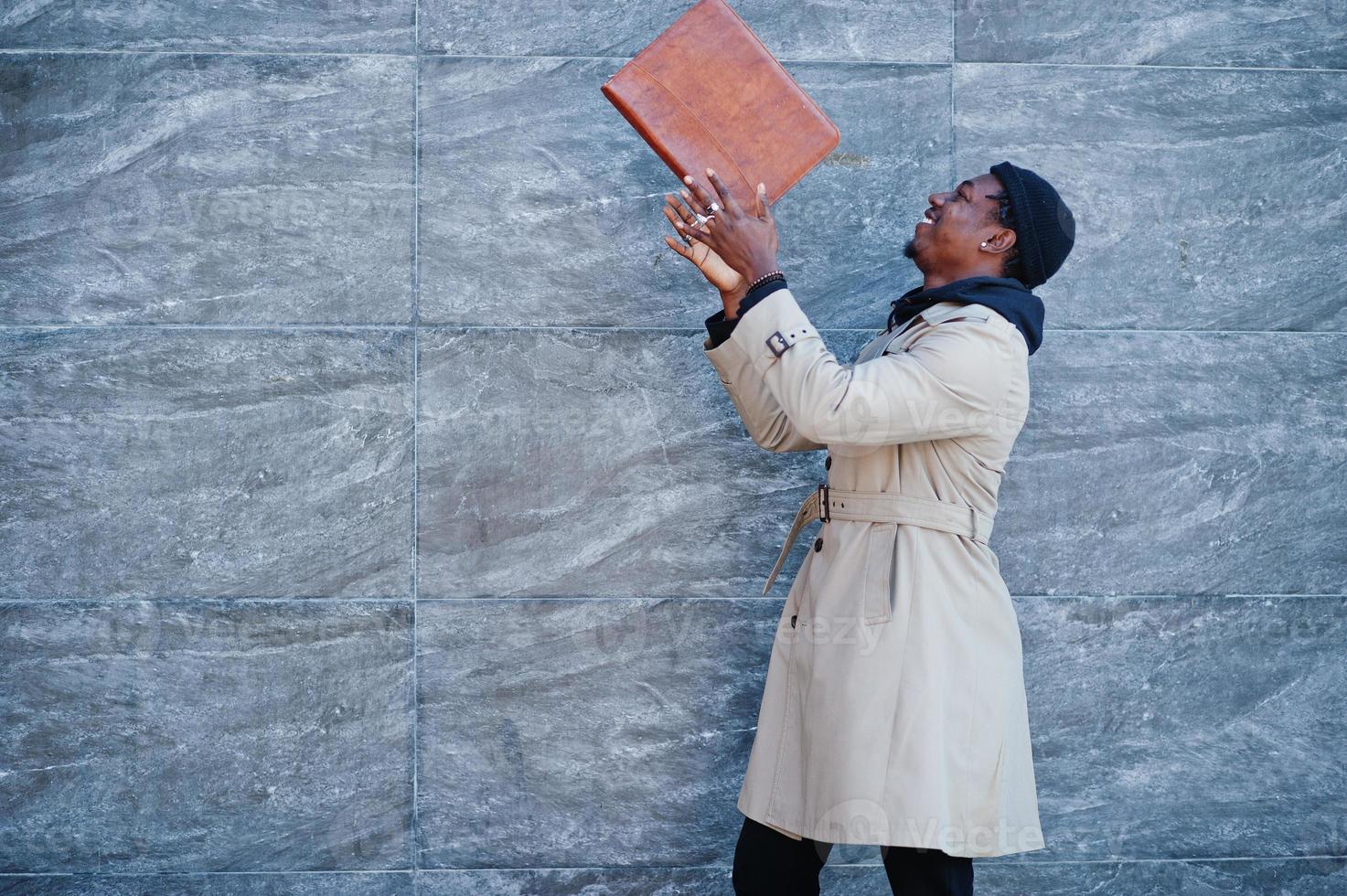 Handsome african american man posing outside in black hat and beige coat with folder in hand. photo