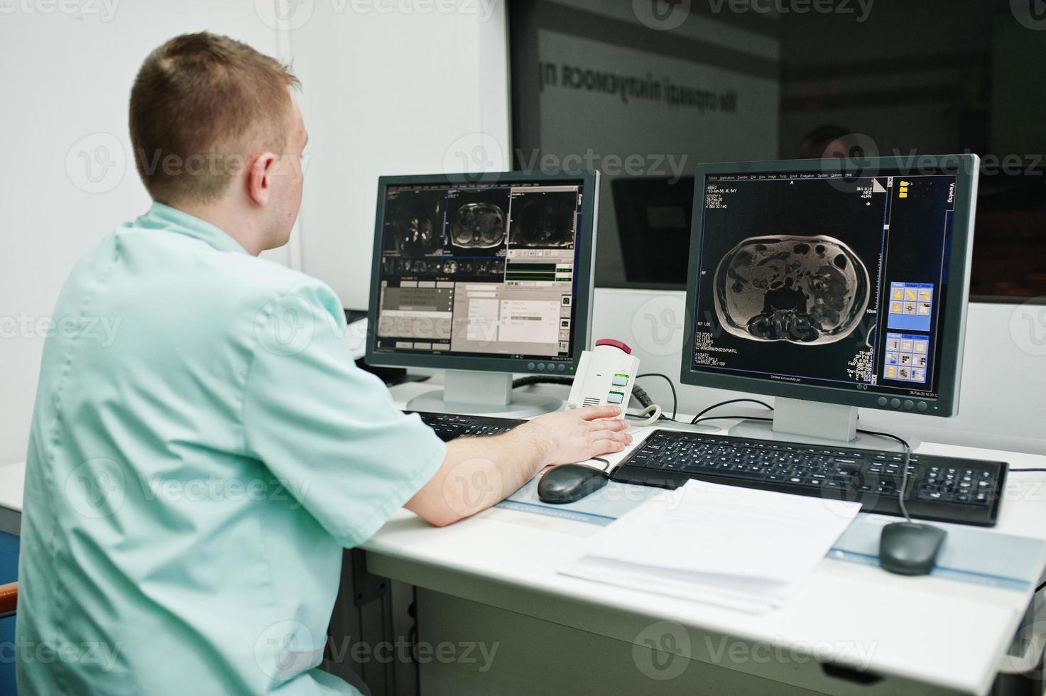 Medical theme. Doctor in the mri office at diagnostic center in hospital, sitting near monitors of computer with human brain on it. photo