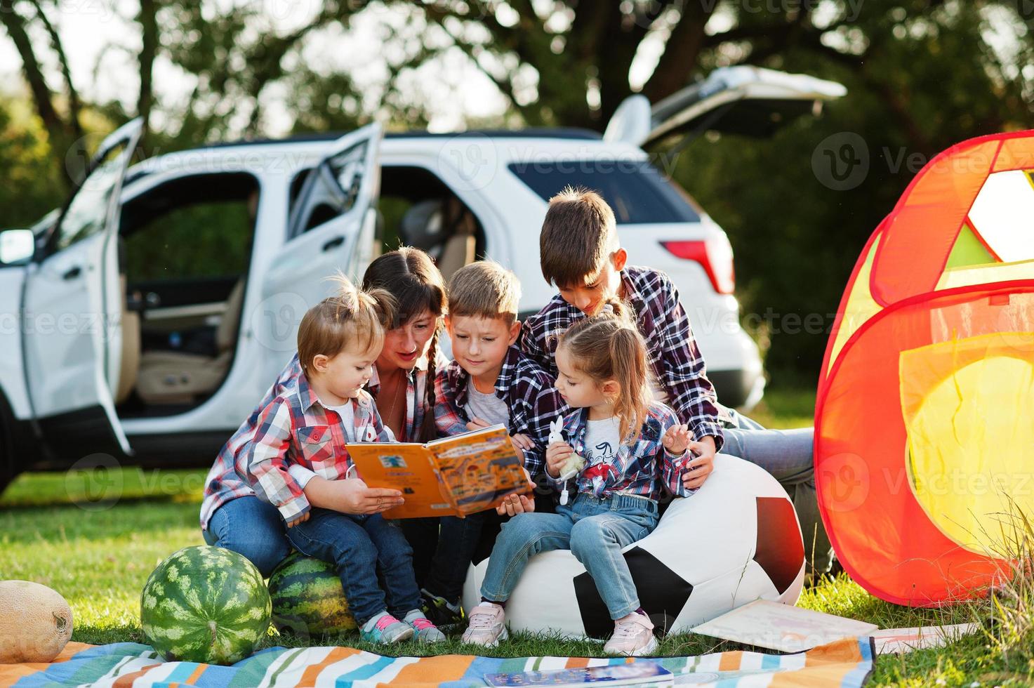 Family spending time together. Mother reading book outdoor with kids against their suv car. photo