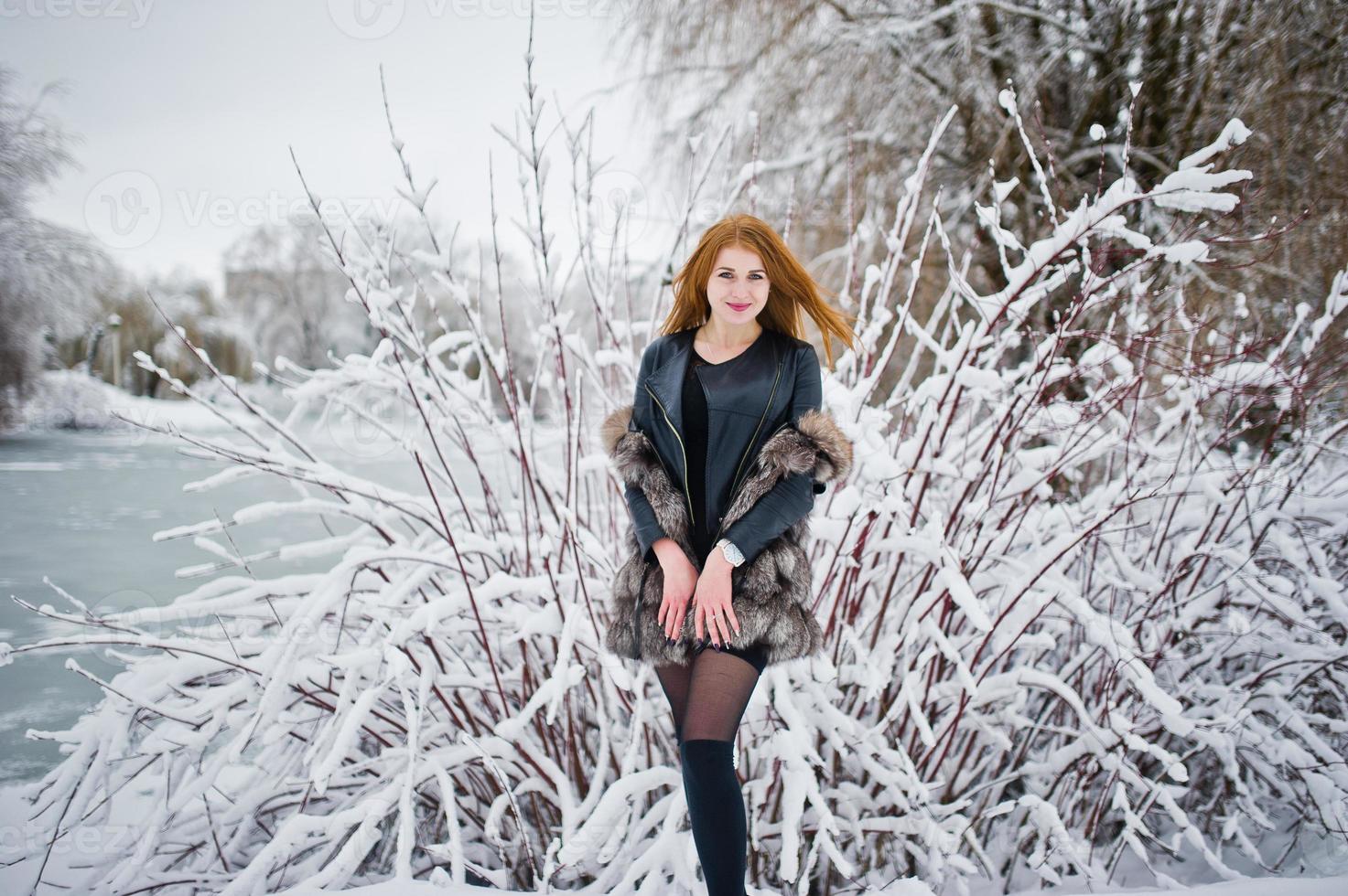 chica pelirroja con abrigo de piel caminando en el parque nevado de invierno. foto