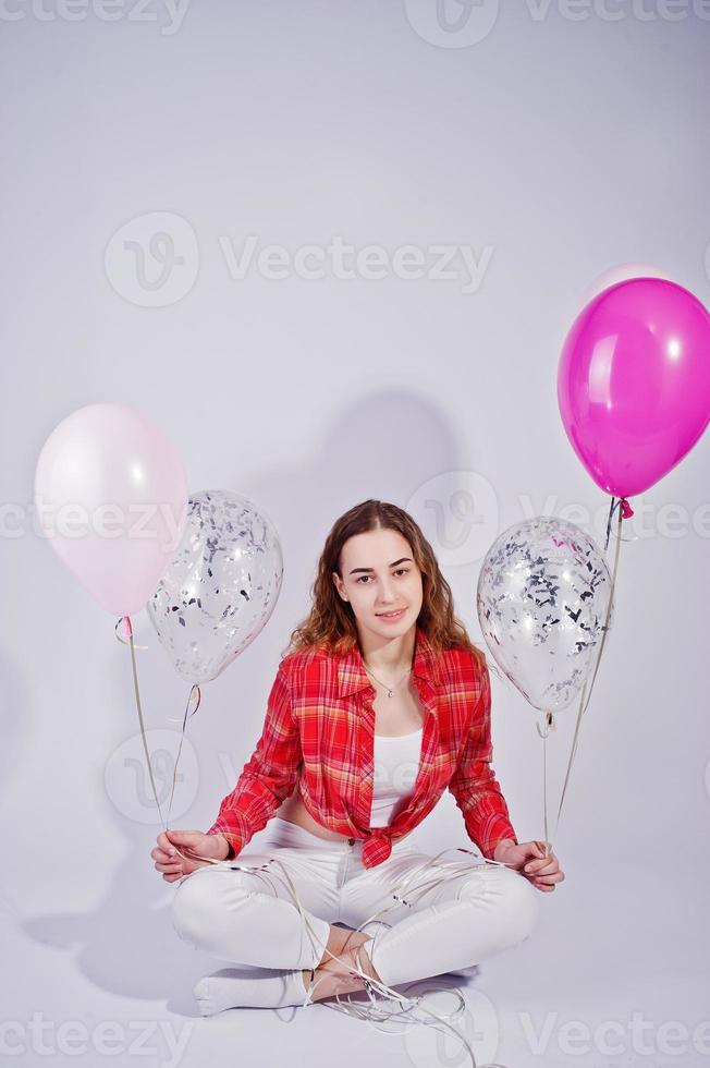 Young girl in red checked shirt and white pants with balloons against white background on studio. photo