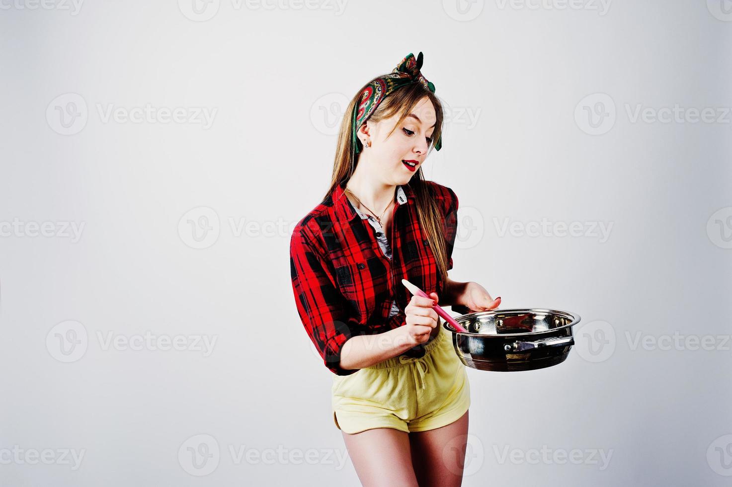 joven ama de casa divertida en camisa a cuadros y pantalones cortos amarillos pin up estilo con sartén aislado sobre fondo blanco. foto