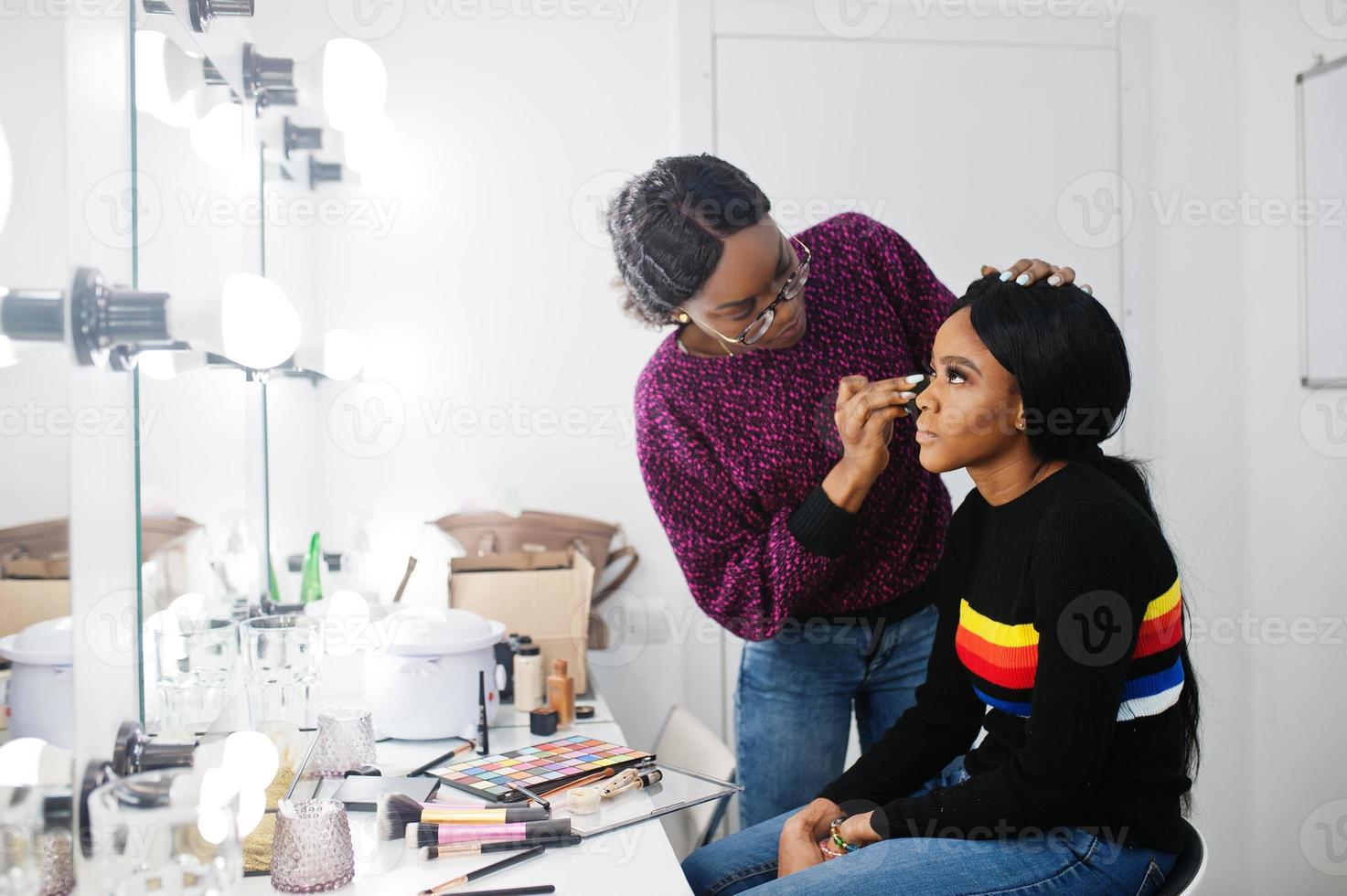 African American woman applying make-up by make-up artist at beauty saloon. photo