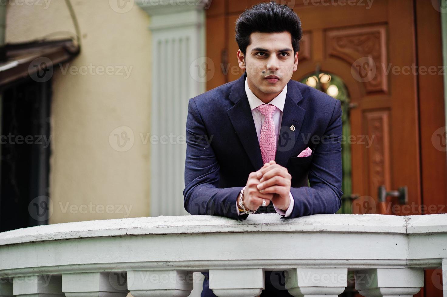 Elegant indian macho man model on suit and pink tie leaned on the railing. photo