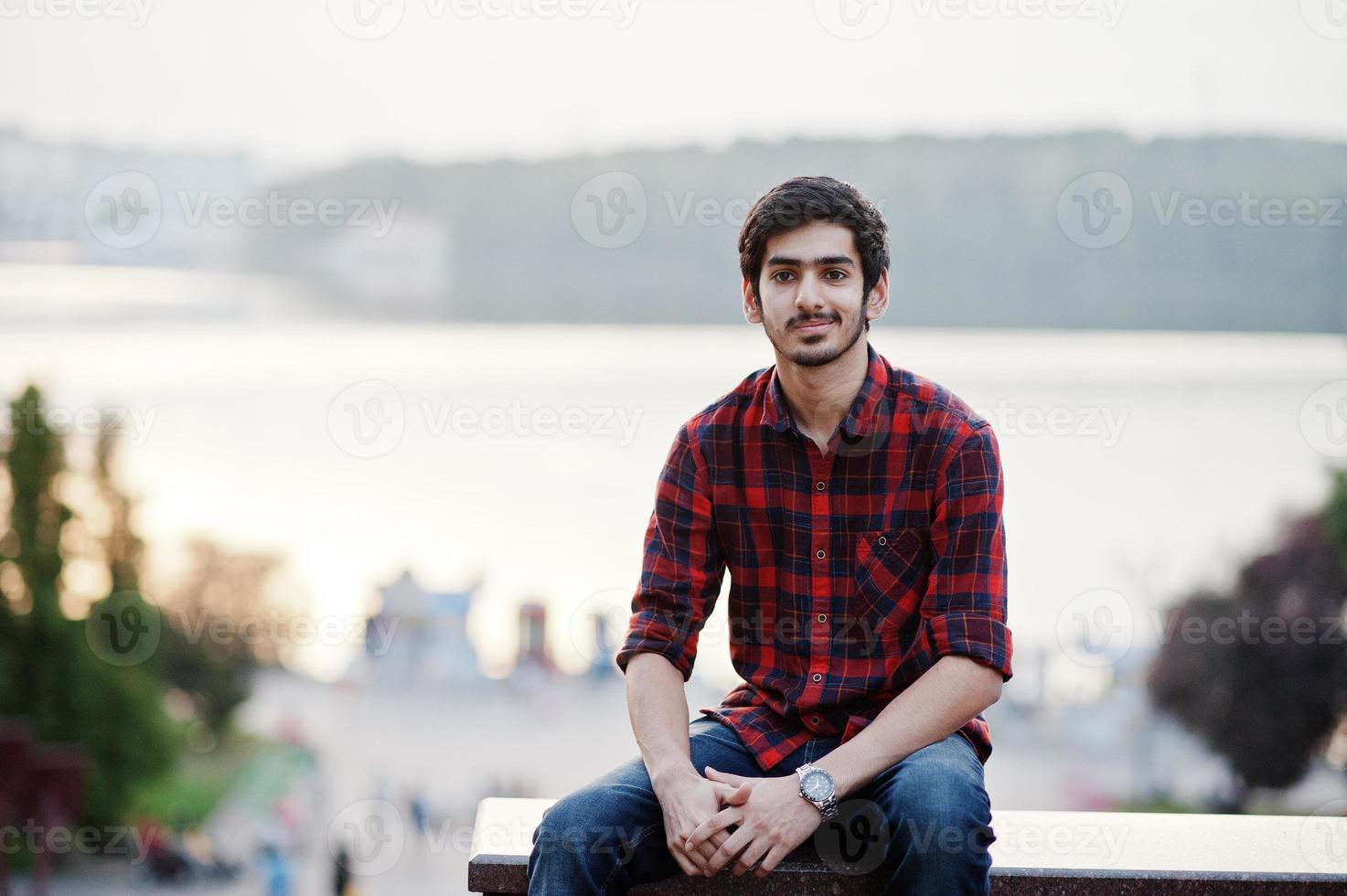 Young indian student man at red checkered shirt and jeans posed at city. photo