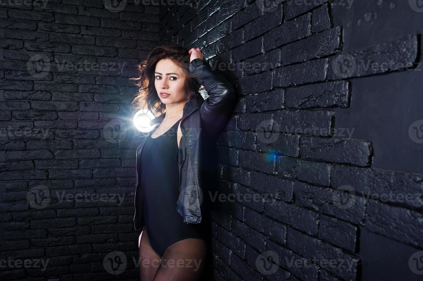 Studio portrait of sexy brunette girl in black leather jacket against brick wall. photo