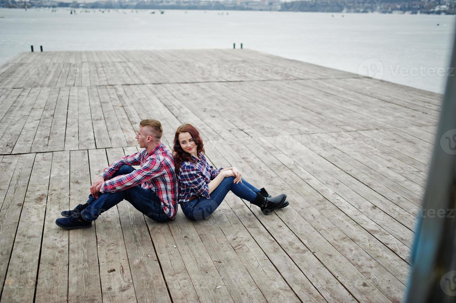 elegante pareja vestida con camisa a cuadros enamorada sentada en el muelle. foto