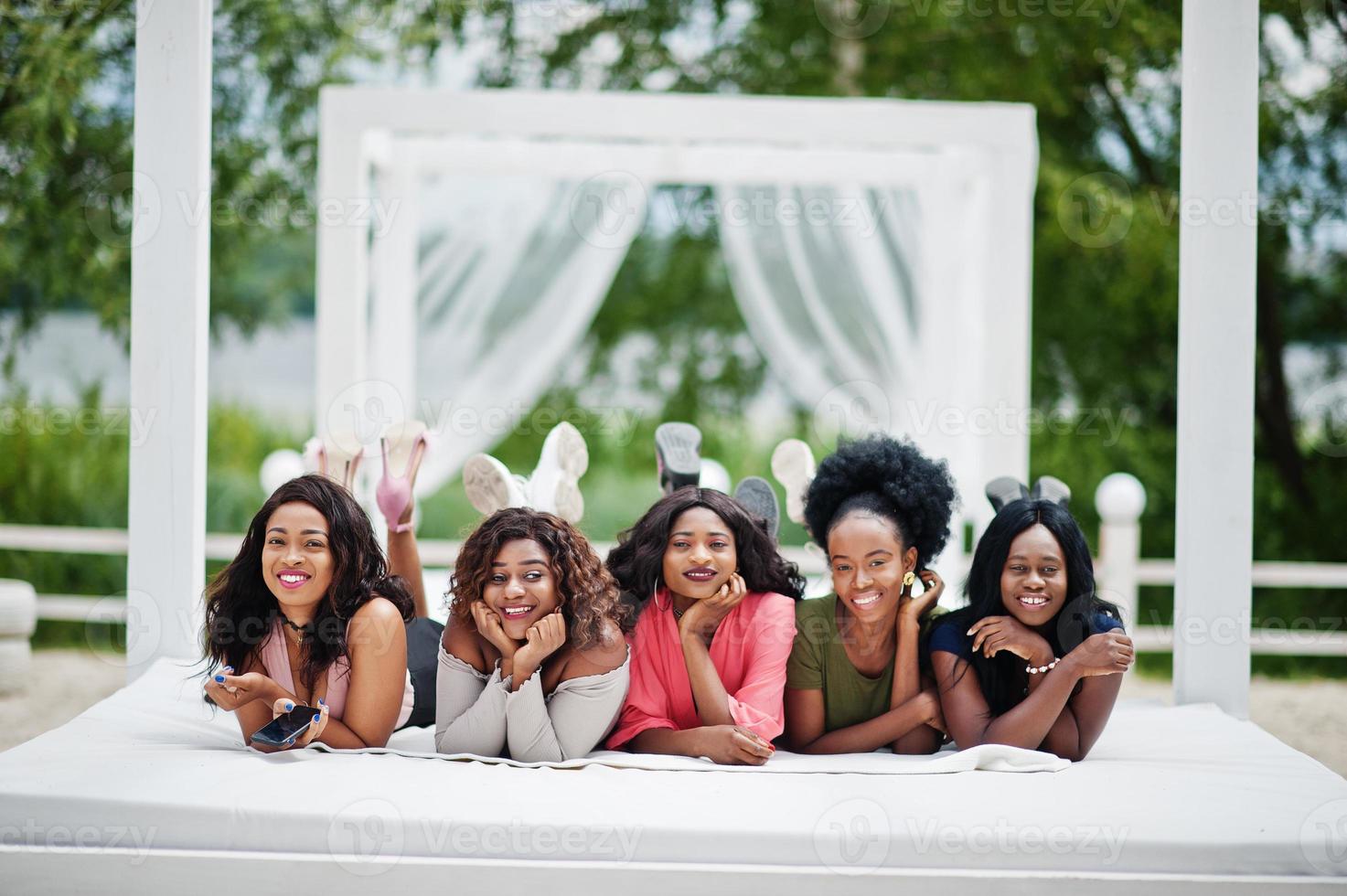 grupo de cinco chicas afroamericanas relajándose en una hermosa cabaña junto a la piscina junto a un complejo de lujo. foto