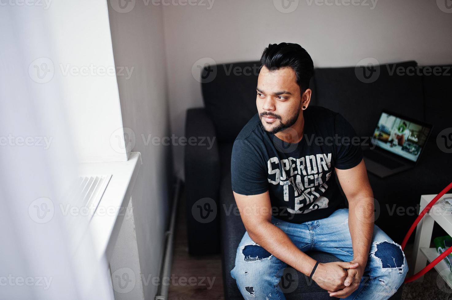 Casual beard indian man sitting at room against laptop. photo