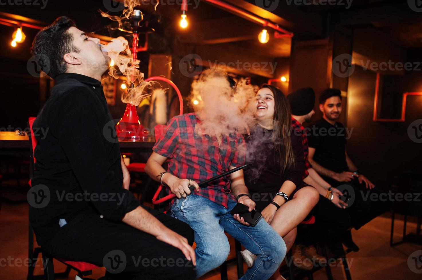 Group of indian friends sitting at lounge bar, smoke hookah and having rest. photo