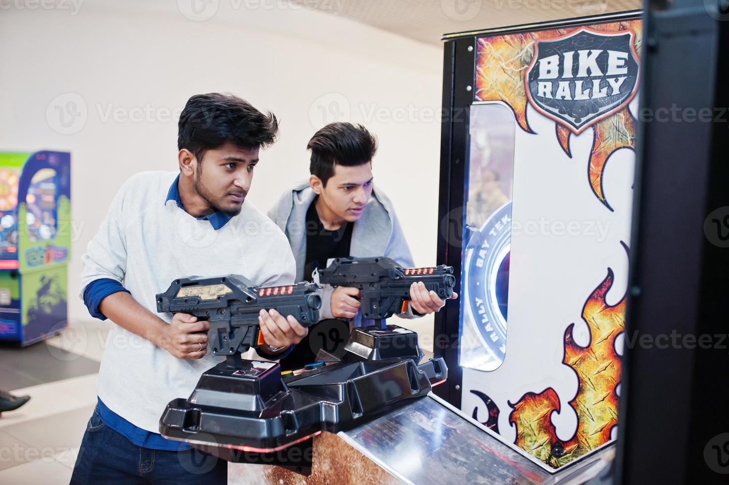 Two asian guys compete on shooter simulator game arcade machine. photo