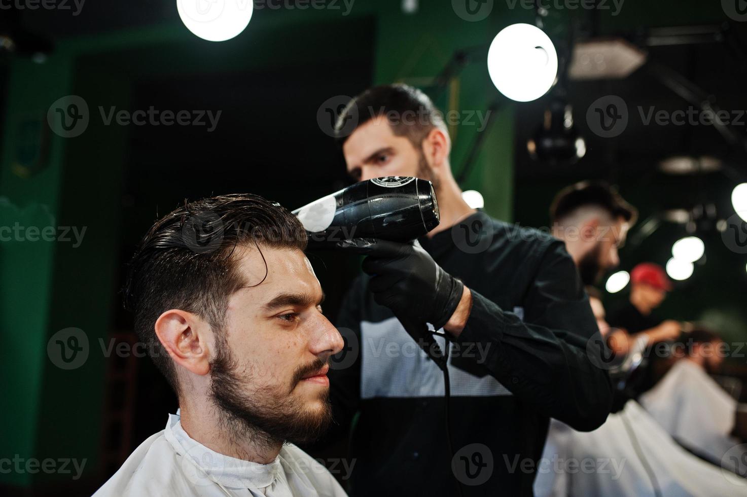 Handsome bearded man at the barbershop, barber at work, using hair dryer. photo