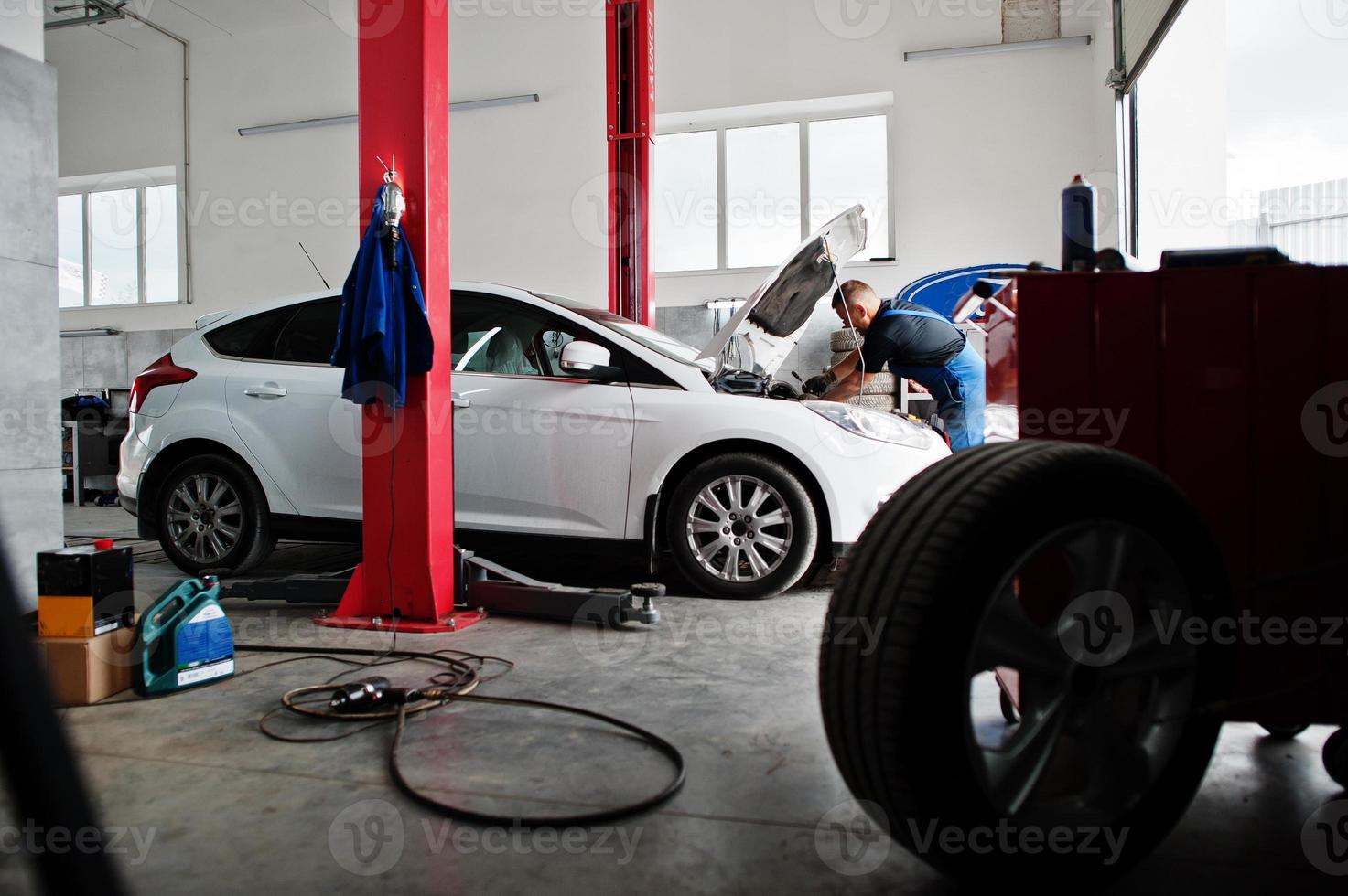 Car repair and maintenance theme. Mechanic in uniform working in auto service, checking engine. photo