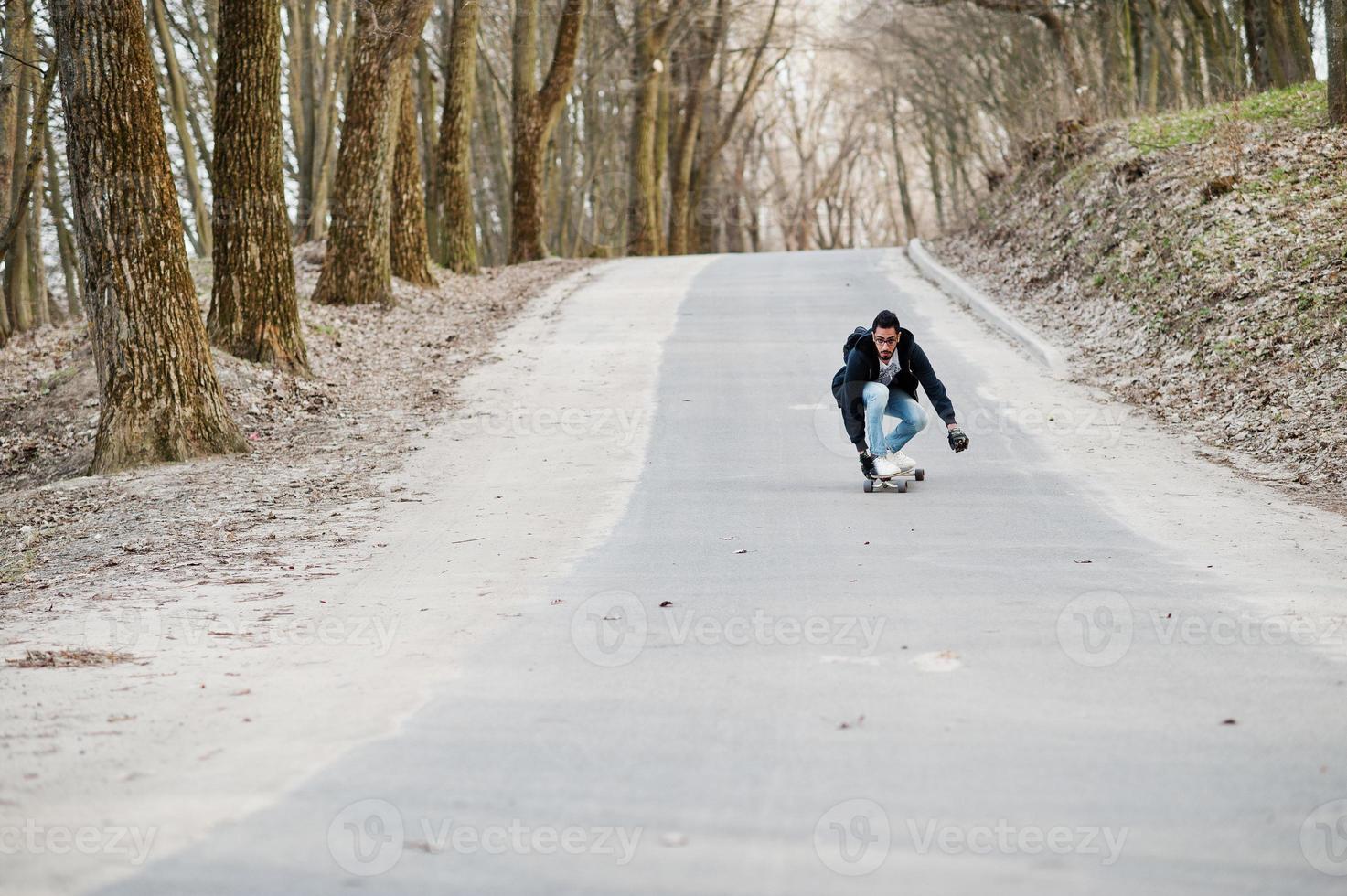 Street style arab man in eyeglasses with longboard longboarding down the road. photo