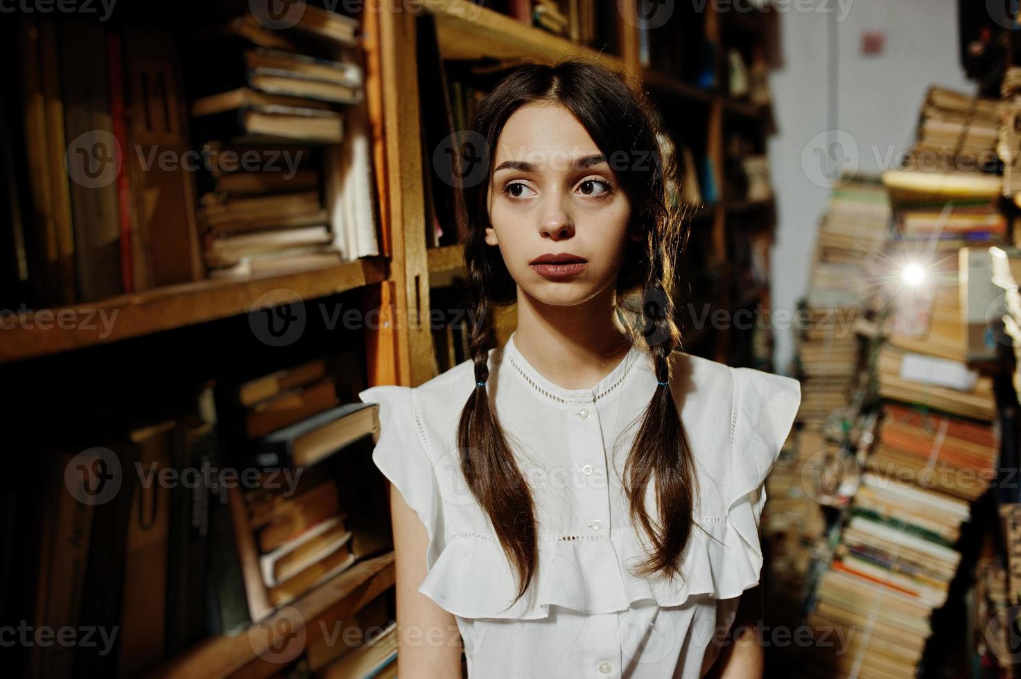 Girl with pigtails in white blouse at old library. photo