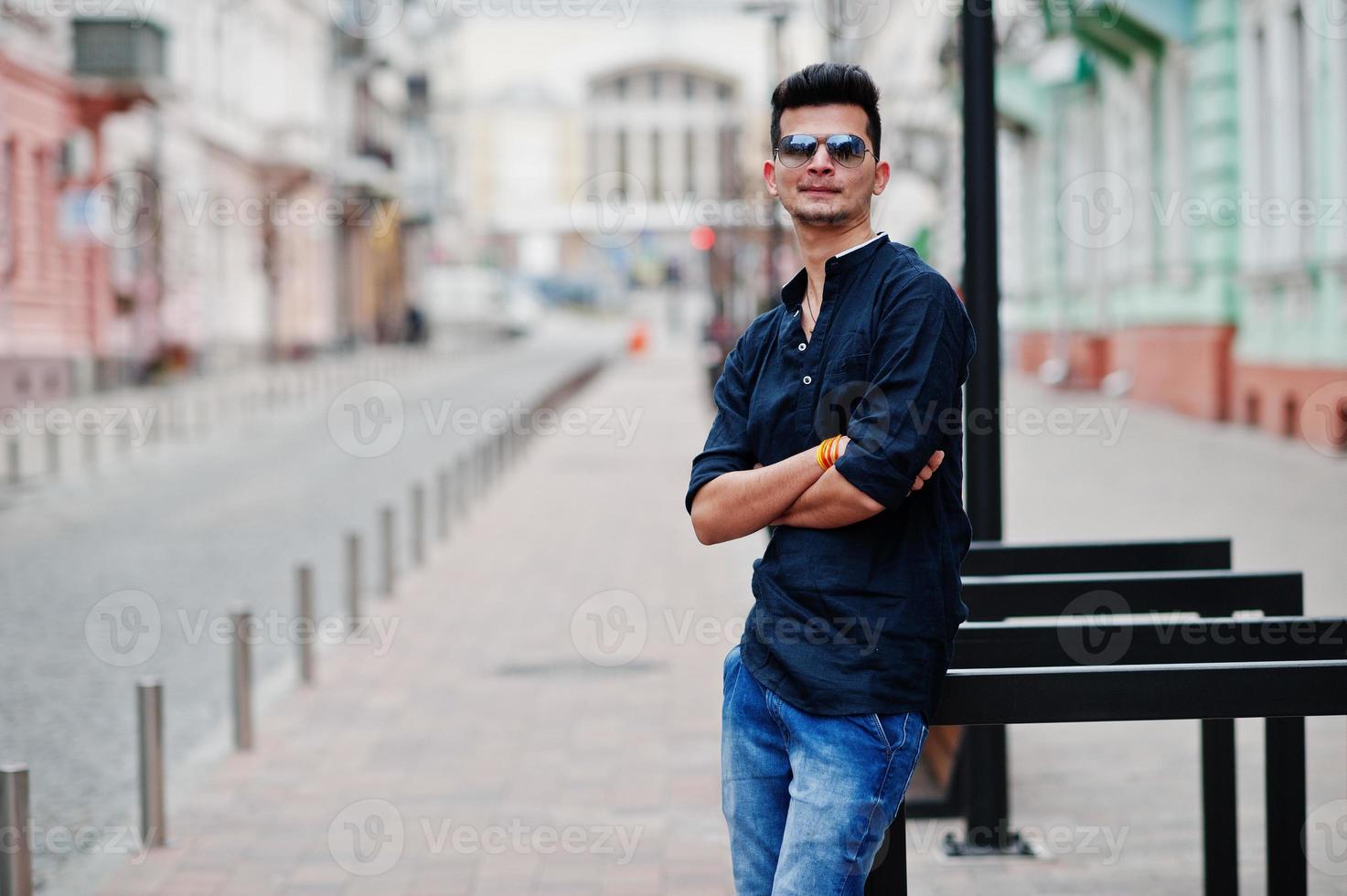 Stylish indian model man in casual clothes, black shirt and sunglasses posed outdoor at street of India. photo