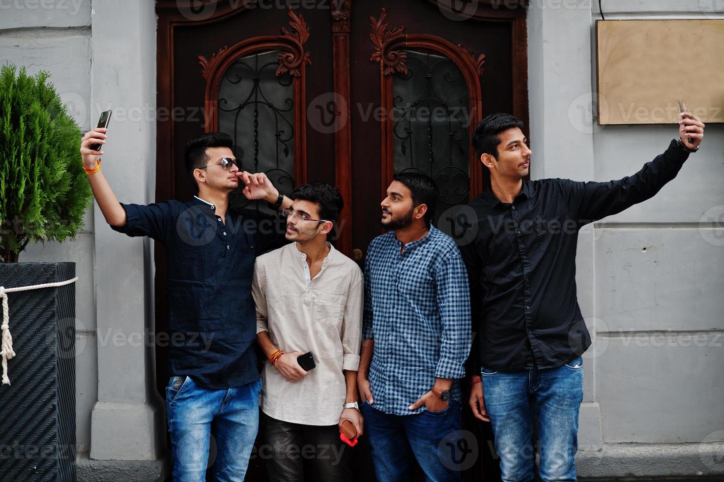 Group of four indian ethnicity friendship togetherness mans. Technology and leisure, guys with phones. Making selfie. photo