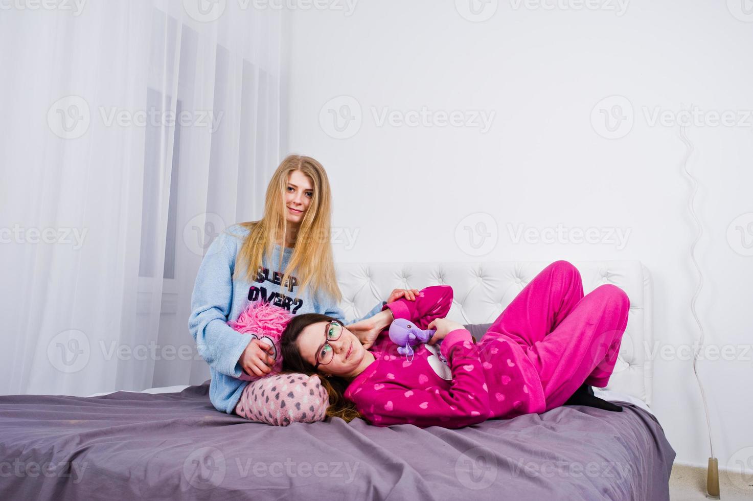 Two friends girls in pajamas having fun on bed at room. photo