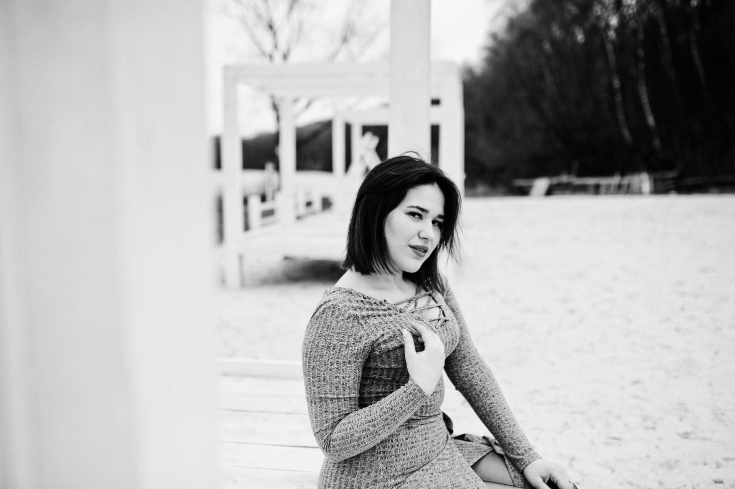 Portrait of brunette girl in gray dress sitting at white wooden construction. photo