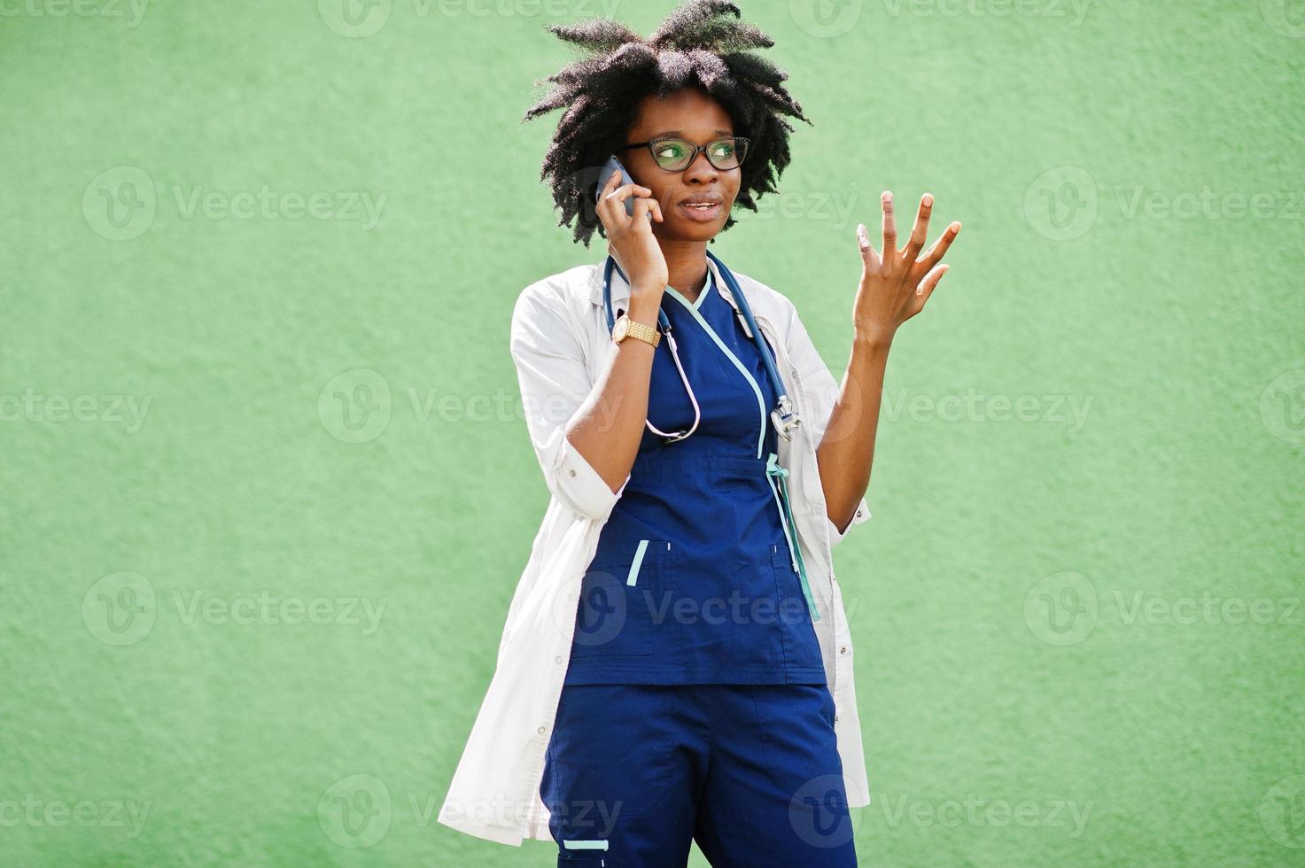 retrato de una doctora afroamericana con estetoscopio usando bata de laboratorio, hablando por teléfono móvil. foto