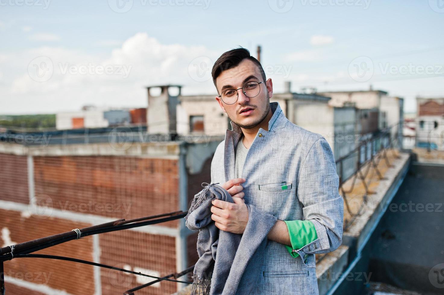 Dreamer stylish macho man in gray suit and glasses posed on the roof. photo