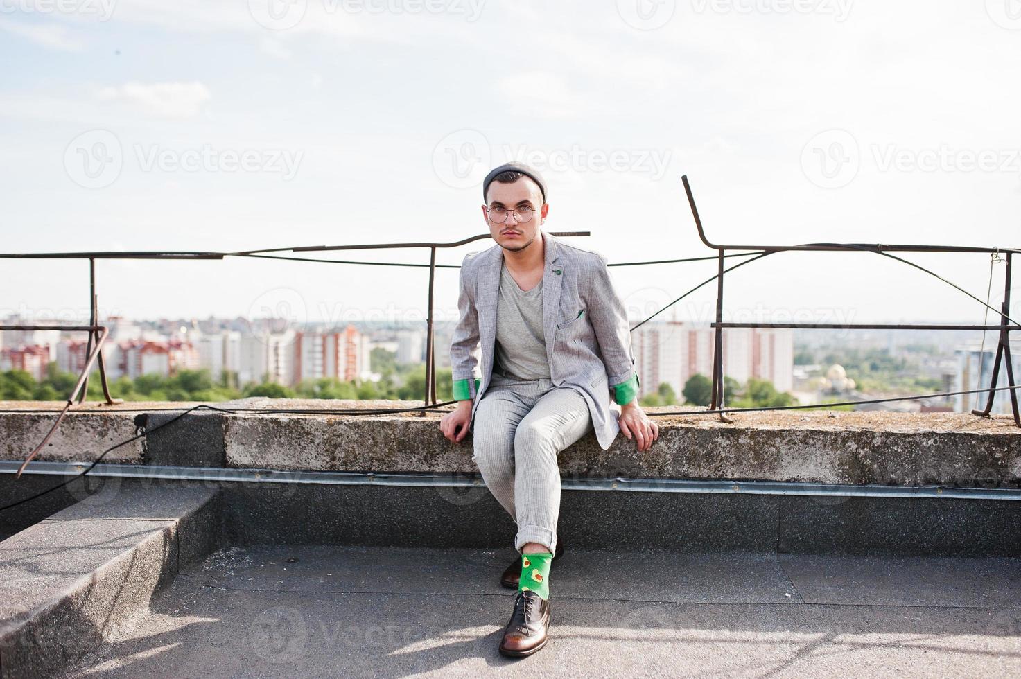 Dreamer stylish macho man in gray suit, hat and glasses posed on the roof. photo