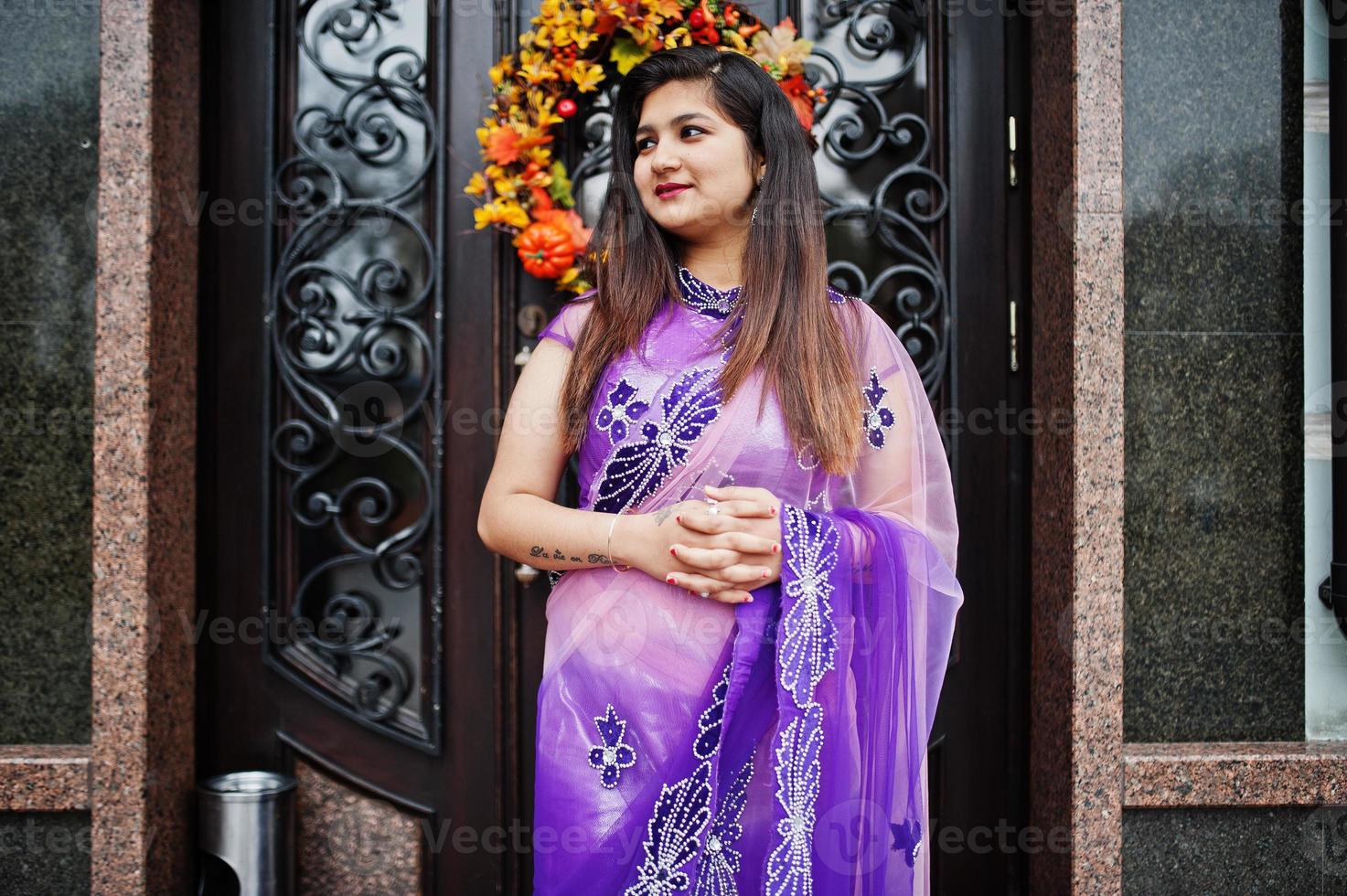 Indian hindu girl at traditional violet saree posed at street against door of restaurant with autumn mood and pumpkins. photo