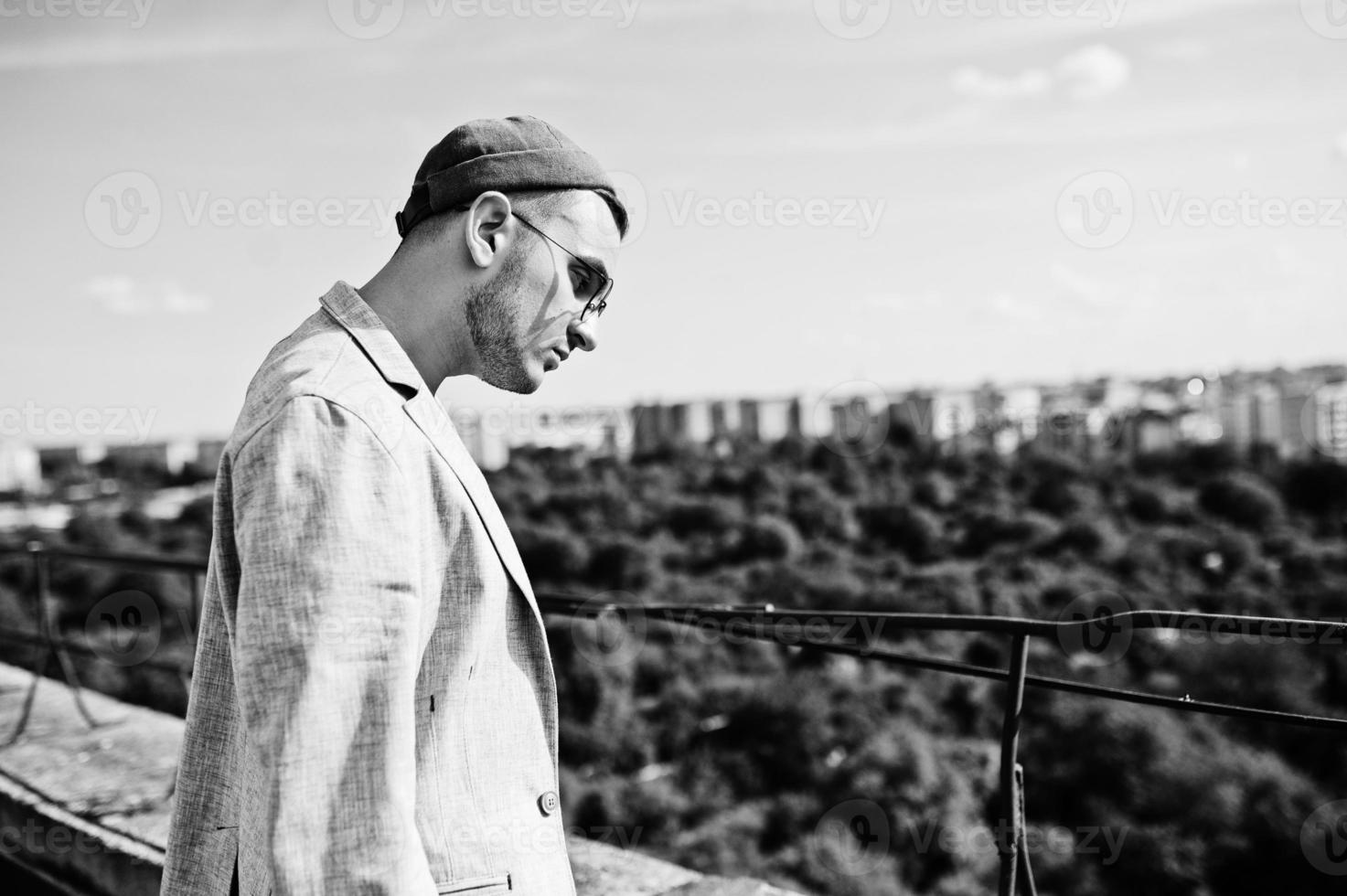 Dreamer stylish macho man in gray suit, hat and glasses posed on the roof. photo