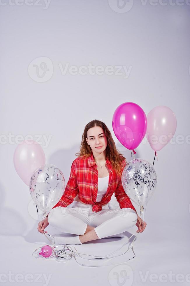 Young girl in red checked shirt and white pants with balloons against white background on studio. photo