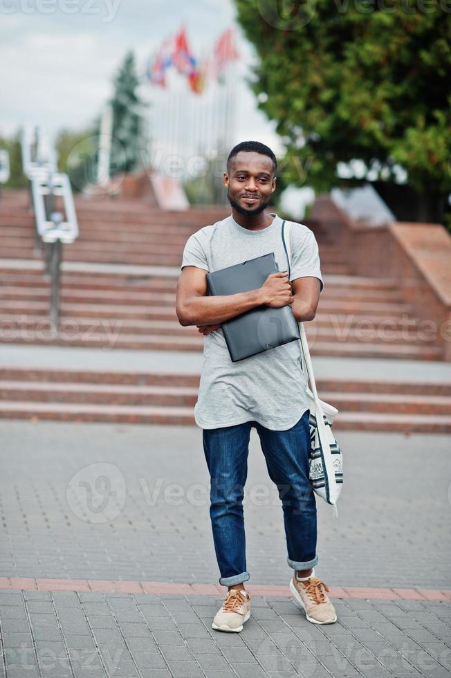 African student male posed with backpack and school items on yard of university, against flags of different countries. photo