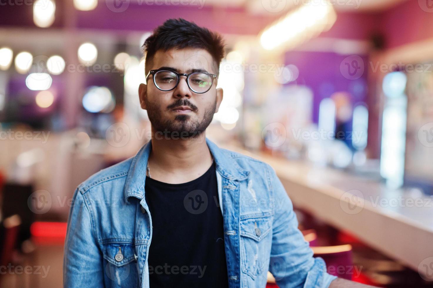 Stylish asian man wear on jeans jacket and glasses posed against bar in club. photo