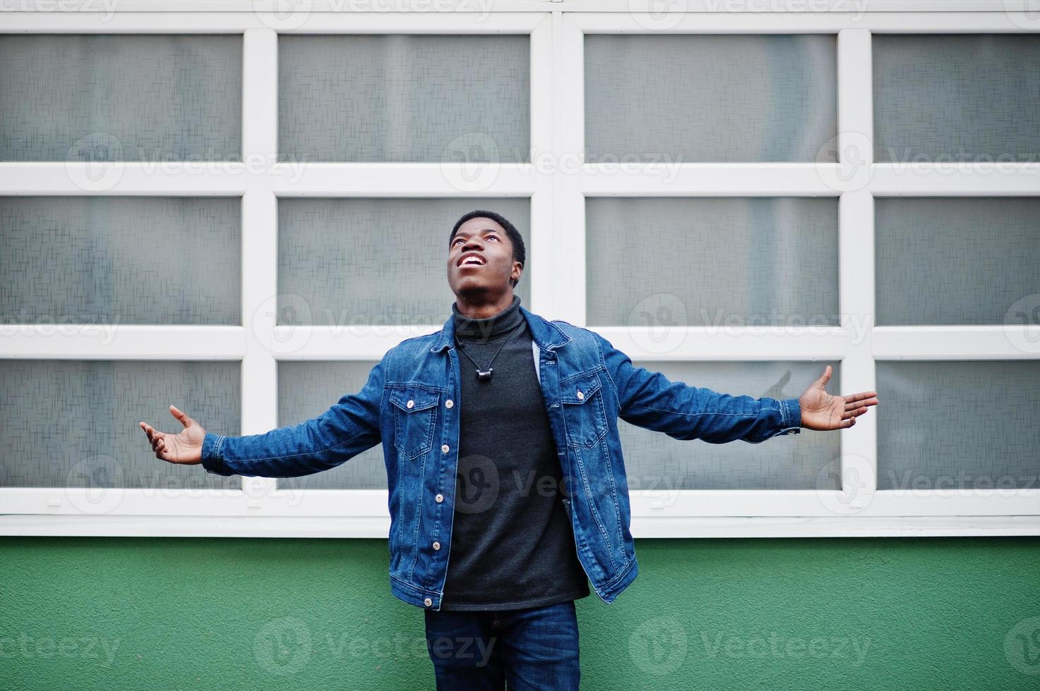 African nigerian man posed outdoor raise hands up against green and white background. photo