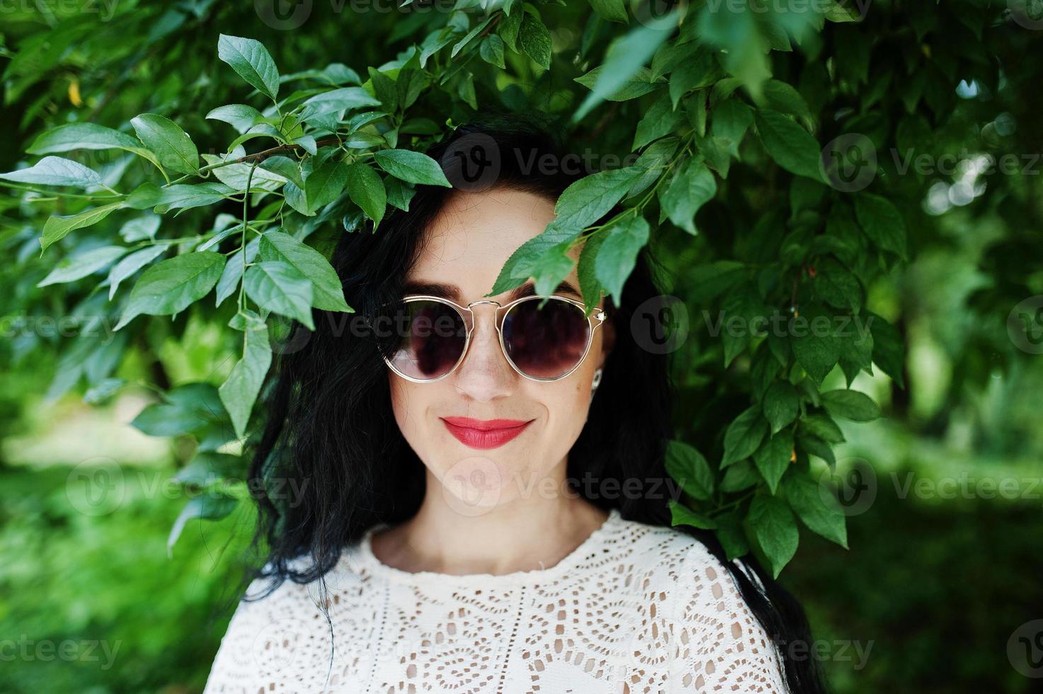 chica morena de blusa blanca con gafas de sol posadas en el parque. foto