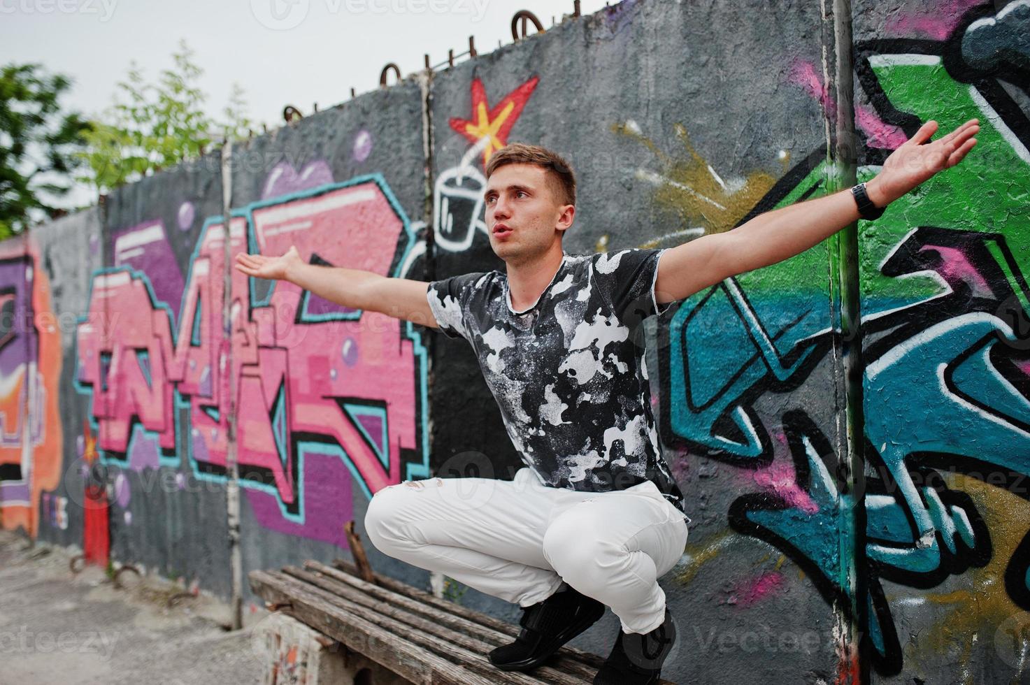 Lifestyle portrait of handsome man posing on the street of city with graffiti wall. photo