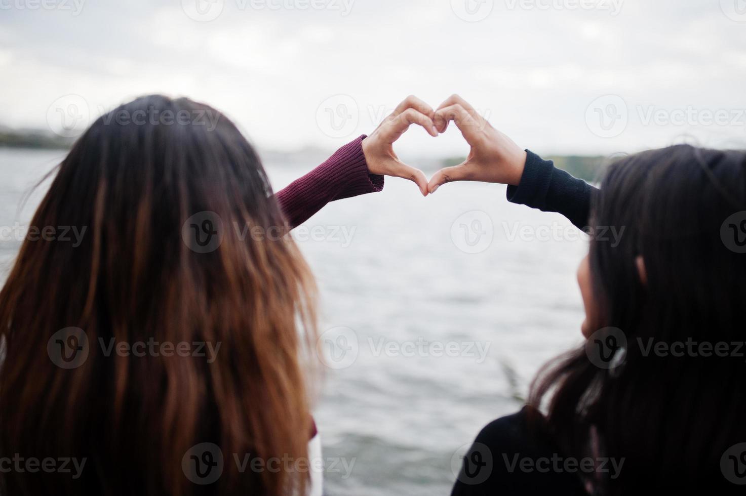 Portrait of back two young beautiful indian or south asian teenage girls in dress show heart by hands. photo