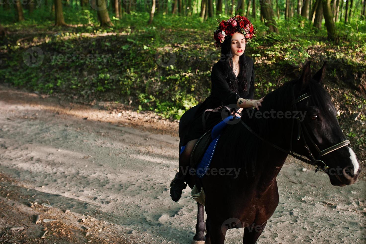 Mystical girl in wreath wear in black at horse in wood. photo