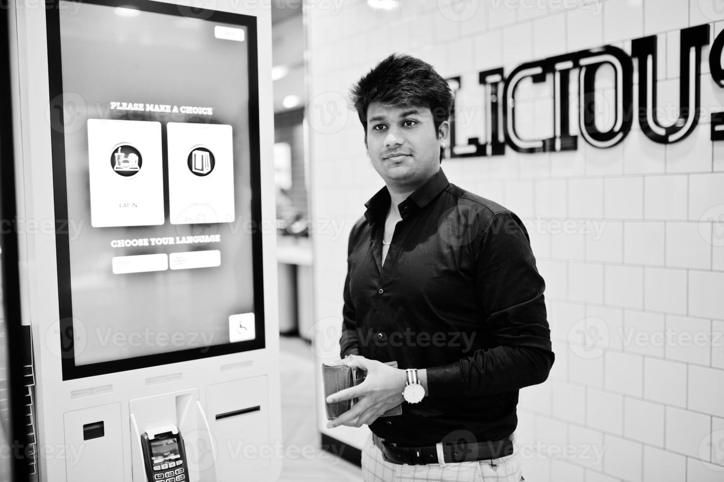 Indian man customer at store place orders and pay through self pay floor kiosk for fast food, payment terminal. Make a choise of language on screen. photo