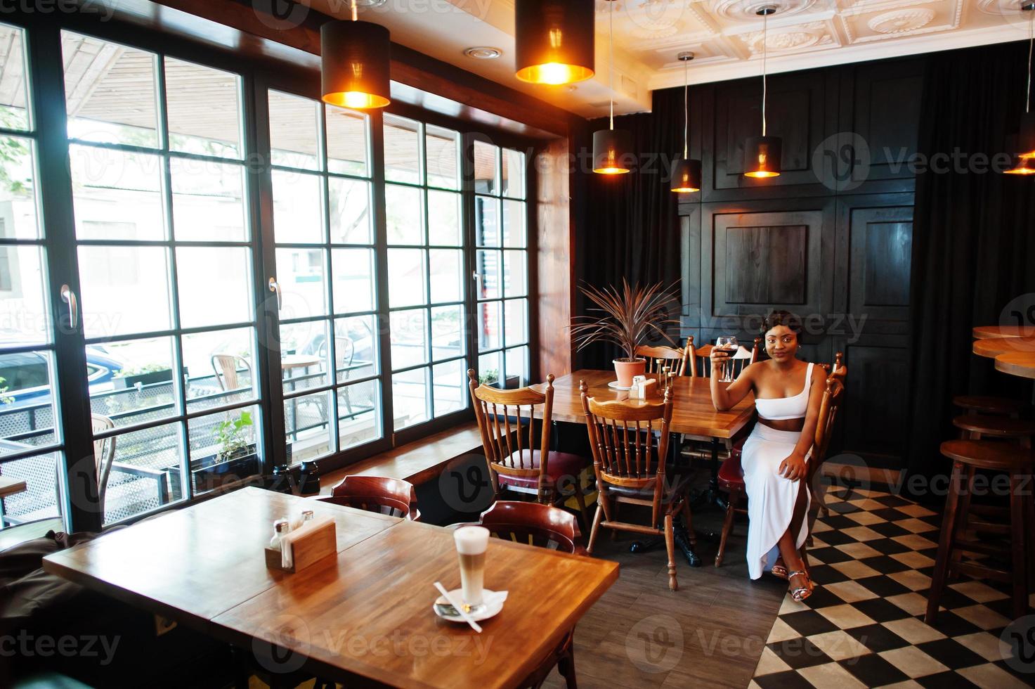 African american woman, retro hairstyle in white dress at restaurant with glass of wine. photo