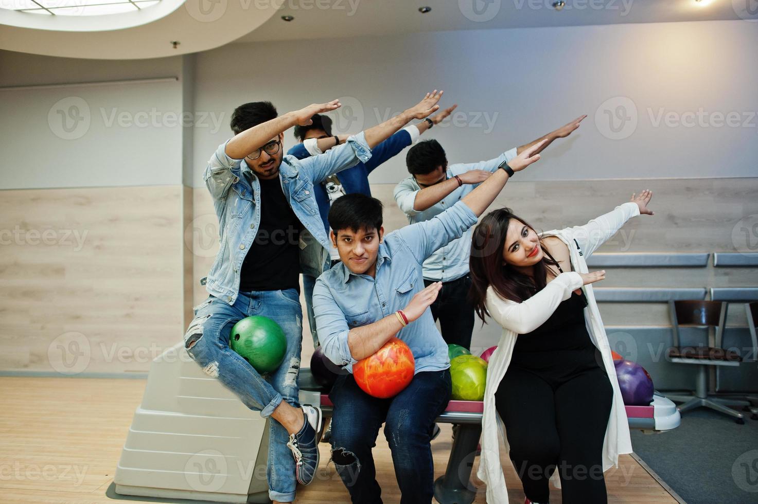 grupo de cinco pueblos del sur de asia descansando y divirtiéndose en el club de bolos. sosteniendo bolas de bolos en las manos y mostrando dab. foto