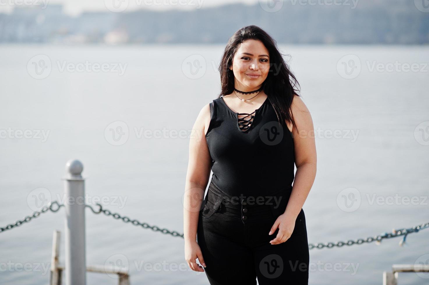 bonita chica modelo latina de ecuador vestida de negro posada contra el lago. foto