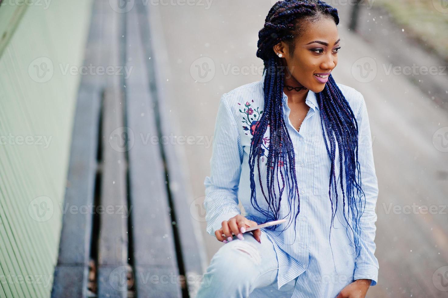 Stylish african american girl with dreads holding mobile phone at hand, outdoor snowy weather. photo